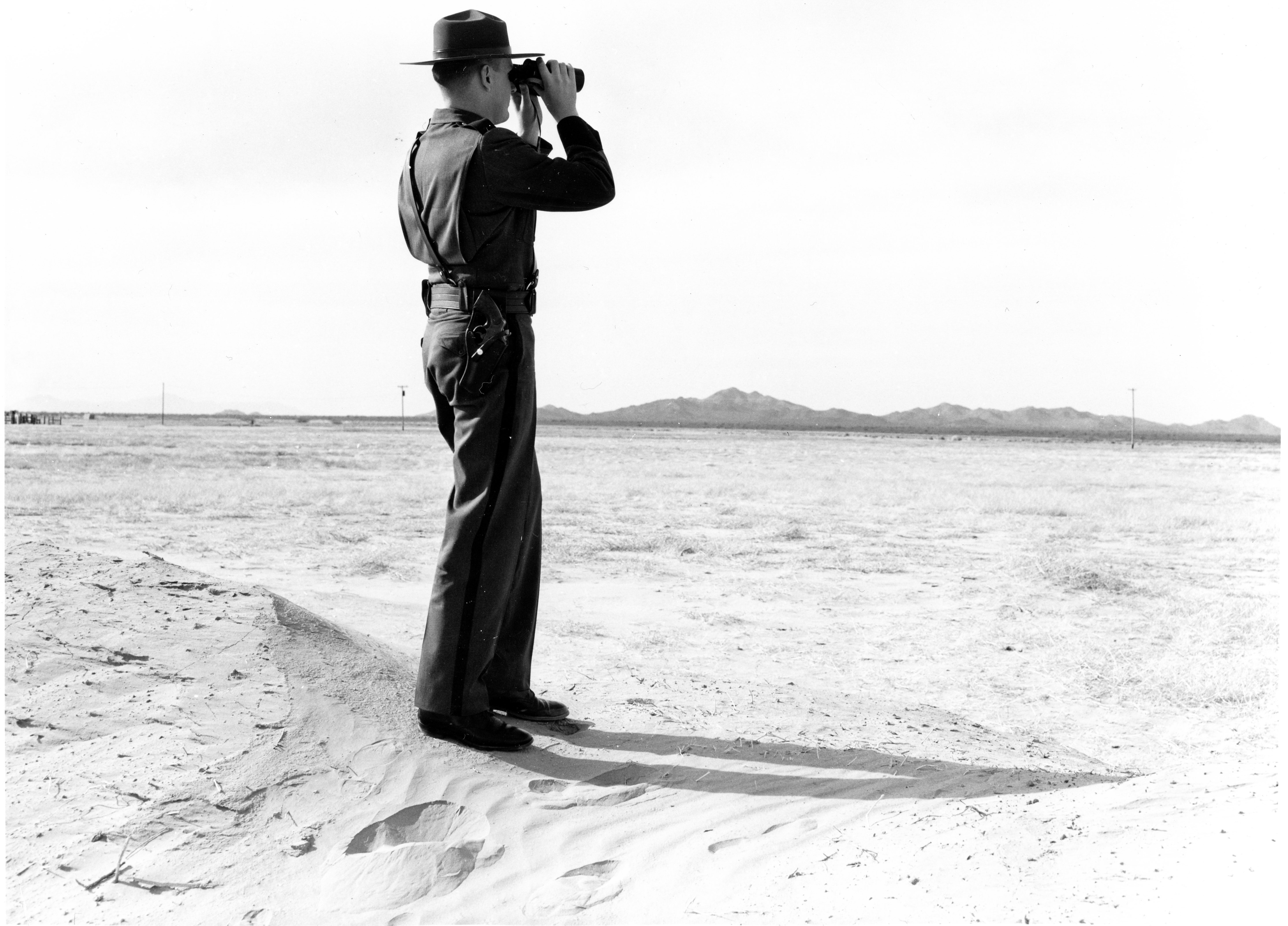 Picture of a border patrol inspector looking through binoculars in a desert landscape
