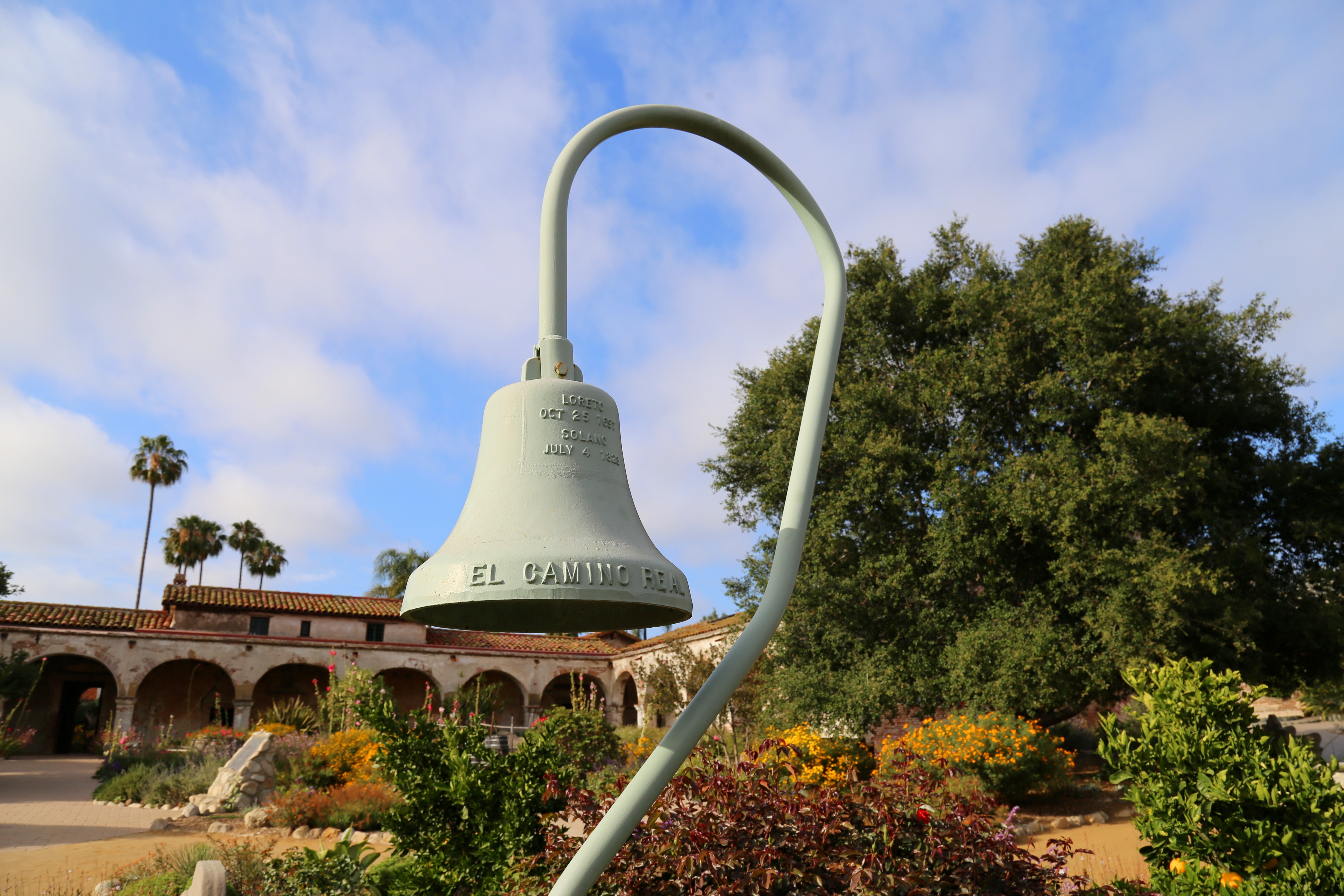 A picture of San Juan Mission's Camino Real Bell in the foreground with the mission in the background